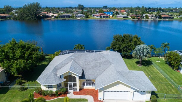 A single-story house with a large garage, surrounded by a well-maintained lawn and palm trees, near a body of water. - Exclusive Villa Fantastic Lakeview, Pool & Spa, Breathtaking Sunset (Cape Coral)