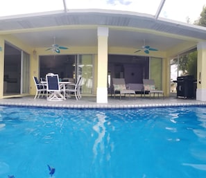 Un área de piscina techada con sillones de descanso y una mesa, además de un ventilador de techo.