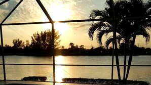 A table with two glasses of wine, a view of the sunset over water, and palm trees. - Exclusive Villa Fantastic Lakeview, Pool & Spa, Breathtaking Sunset (Cape Coral)