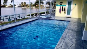 A swimming pool with clear blue water, a small hot tub, and a view of a lake. - Exclusive Villa Fantastic Lakeview, Pool & Spa, Breathtaking Sunset (Cape Coral)