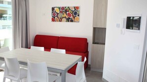 A modern room with a dining table, white chairs, a red sofa, and a colorful spice rack on the wall.