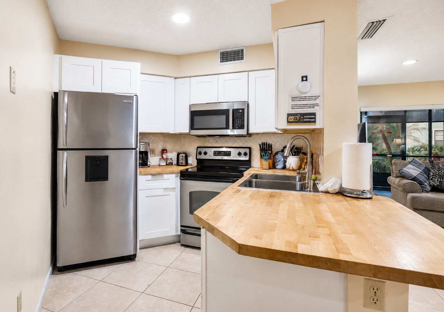 Una cocina moderna con electrodomésticos de acero inoxidable, armarios blancos y encimera de madera.