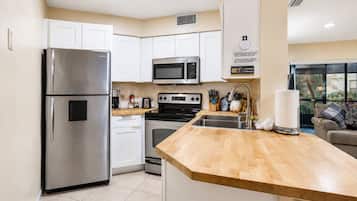 Una cocina moderna con electrodomésticos de acero inoxidable, armarios blancos y encimera de madera.