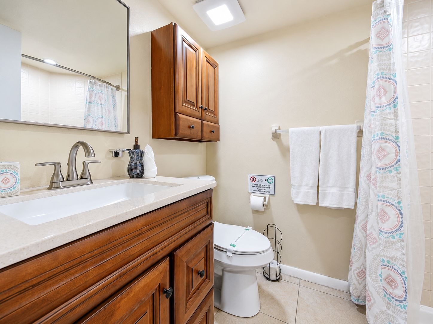 A bathroom with a wooden vanity, a sink, a toilet, and a shower curtain.