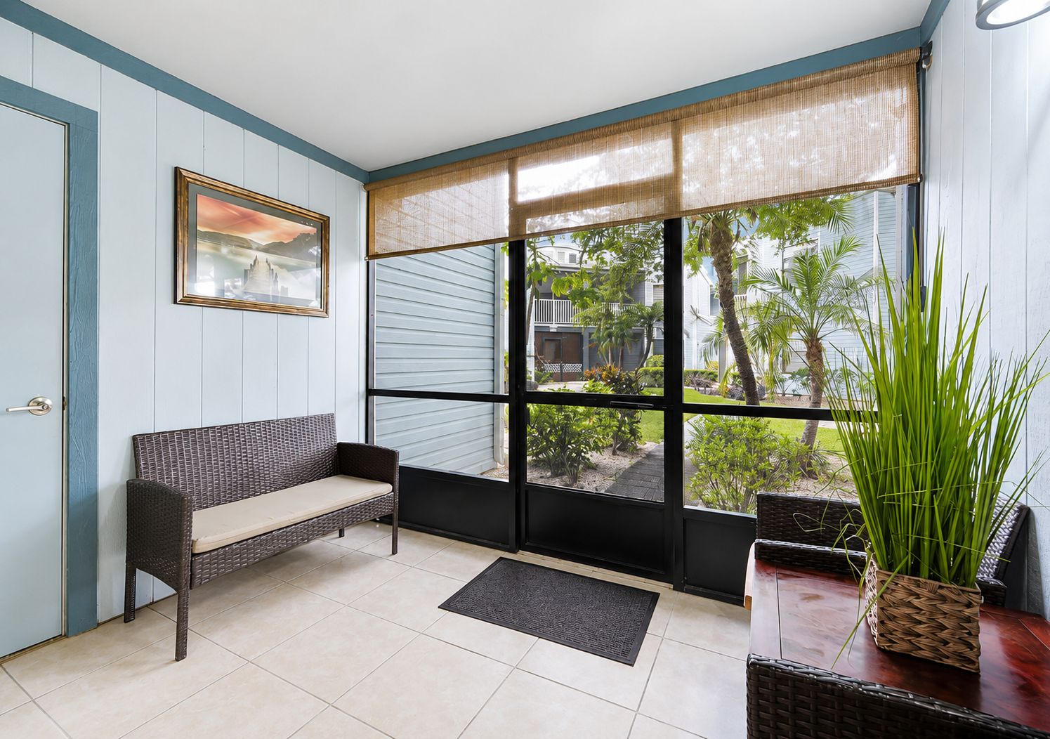 A room with a bench, a potted plant, and a view of a residential area through large windows.