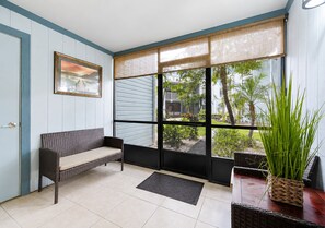 Une pièce avec un banc, une plante en pot et une vue sur un quartier résidentiel, visible à travers de grandes fenêtres.