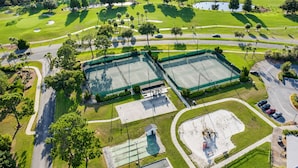 An aerial view of a golf course with multiple tennis courts, a parking area, and surrounding greenery. - Colinas del Atlantico Vacational House 1st Floor (Isabela)
