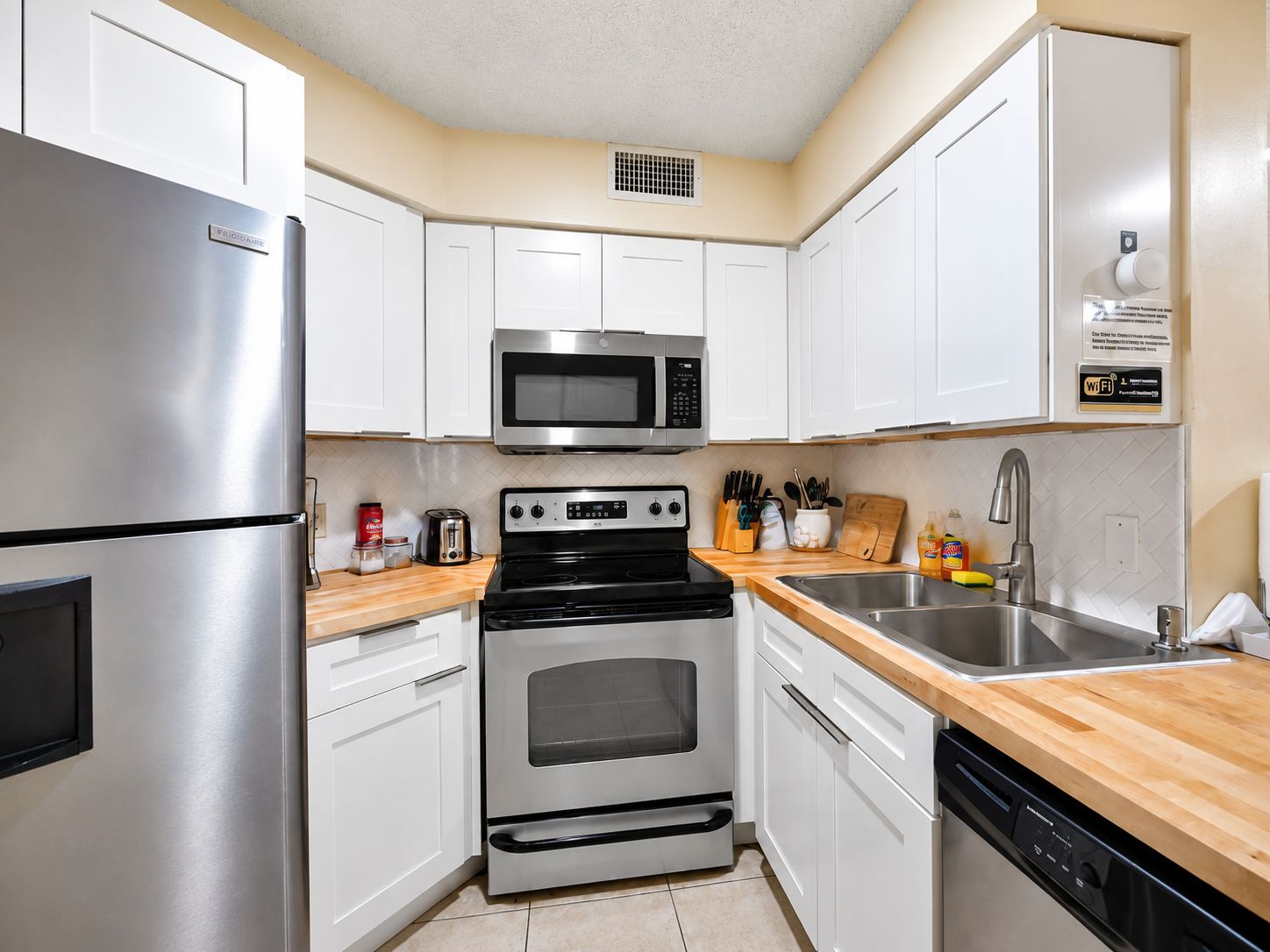 A compact kitchen with white cabinets, a stainless steel refrigerator, a microwave, a stove, and a dishwasher.