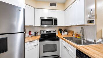 A compact kitchen with white cabinets, a stainless steel refrigerator, a microwave, a stove, and a dishwasher.