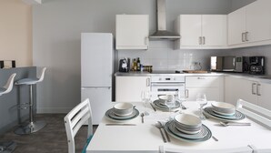 Une cuisine moderne avec des meubles blancs, un réfrigérateur en acier inoxydable et un coin repas agrémenté d ’assiettes, de verres et de couverts.