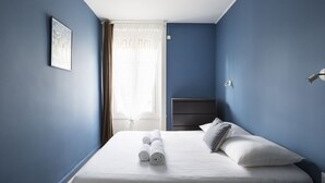 Un lit bien fait, avec des draps blancs et des serviettes pliées, une table de chevet et une tête de lit.
