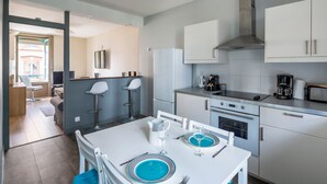 Une cuisine moderne avec des armoires blanches, une hotte en acier inoxydable et un coin repas avec une table blanche mise pour deux personnes.