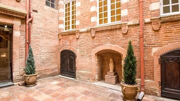 A courtyard with brick walls, two large doors, and potted evergreen trees.