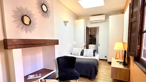 A compact hotel room with a bed, a desk, a chair, a small table, and a mirror.