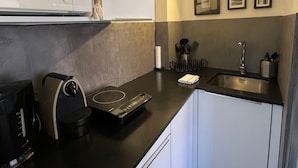 A modern kitchen with a microwave, coffee maker, and a sink. There are framed pictures on the wall and a small window above the microwave.