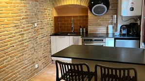 Een kleine keuken met een bakstenen muur, een inbouwoven, een koffieapparaat en twee barkrukken.