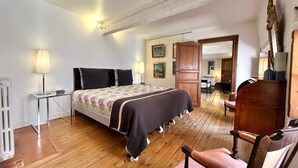 A bedroom with a wooden floor, a bed with a patterned bedspread, a bedside table with a lamp, and a chair. - Le Grand Croix Baragnon (Toulouse)