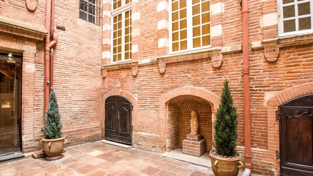A courtyard with brick walls, two large doors, and potted evergreen trees. - Le Grand Croix Baragnon (Toulouse)