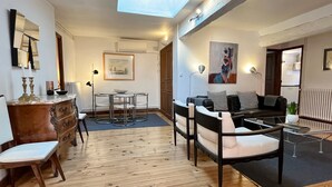 A modern living room with a wooden floor, a dining area with a round table and chairs, a black leather sofa, and a ceiling light. - Le Grand Croix Baragnon (Toulouse)