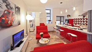 Eine moderne Küche mit roten Akzenten, ein Essbereich mit roter Einrichtung und ein Fernseher im Wohnzimmer.