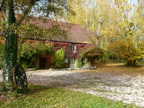 Une maison de campagne au toit rouge, entourée d’arbres aux feuilles d’automne.