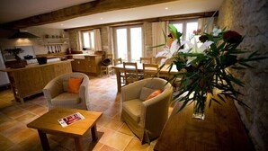 A cozy living area with a wooden dining table, two sofas, and a coffee table. There is a kitchen in the background with wooden cabinets and a window. - Moulin de Cussigny, charming B&B (Corgoloin)
