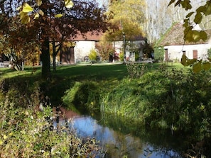 A serene outdoor setting with a small pond, lush greenery, and traditional stone buildings. - Moulin de Cussigny, charming B&B (Corgoloin)