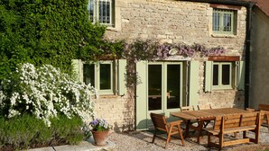 A stone house with a garden patio, a wooden table, and chairs. - Moulin de Cussigny, charming B&B (Corgoloin)