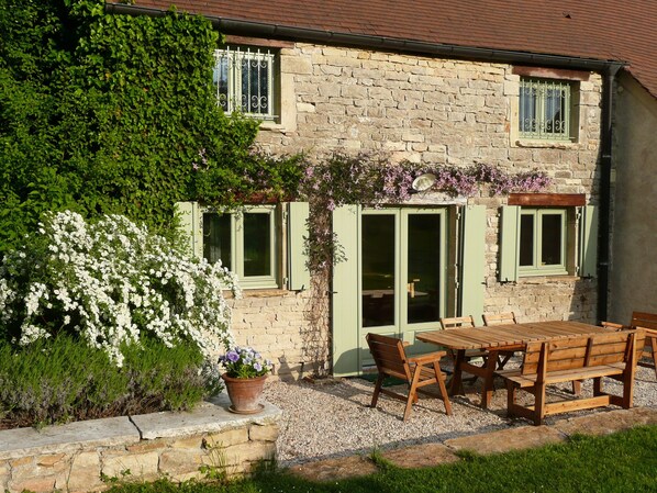 A stone house with a garden patio, a wooden table, and chairs. - Moulin de Cussigny, charming B&B (Corgoloin)