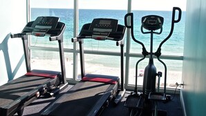 Ein Fitnessraum mit Laufbändern und Crosstrainern mit Blick auf einen Strand.