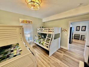 A child's bedroom with bunk beds, a desk, and a window with blinds.