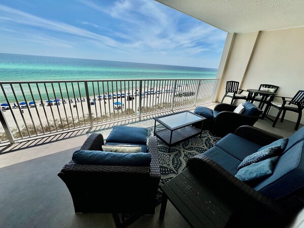 A balcony with a view of the beach and ocean. There are lounge chairs and a small table.