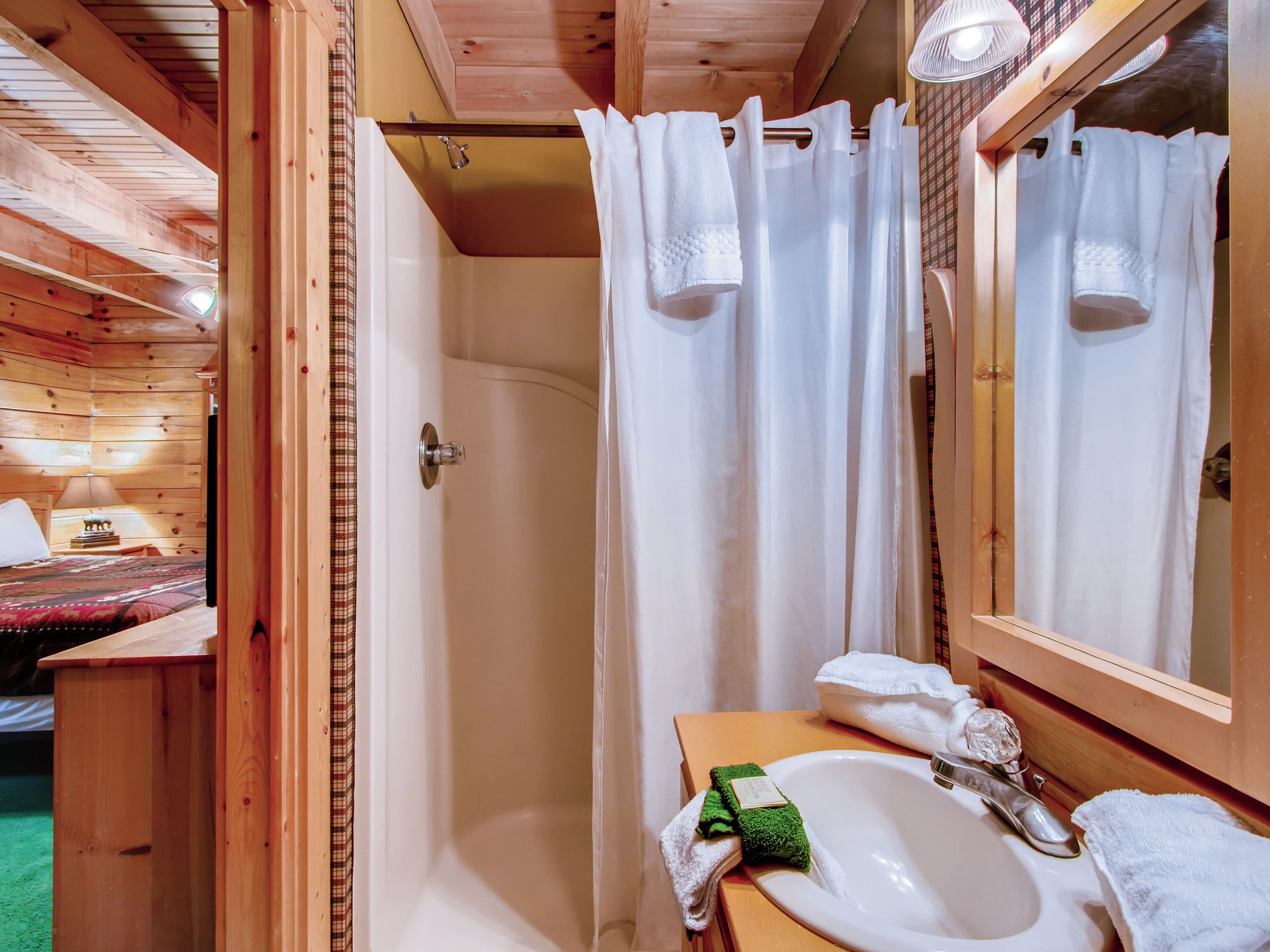 A wooden cabin bathroom with a shower, a sink, and a mirror.