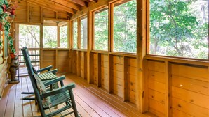 Una cabaña de madera con un porche, ventanas amplias y vistas al bosque.