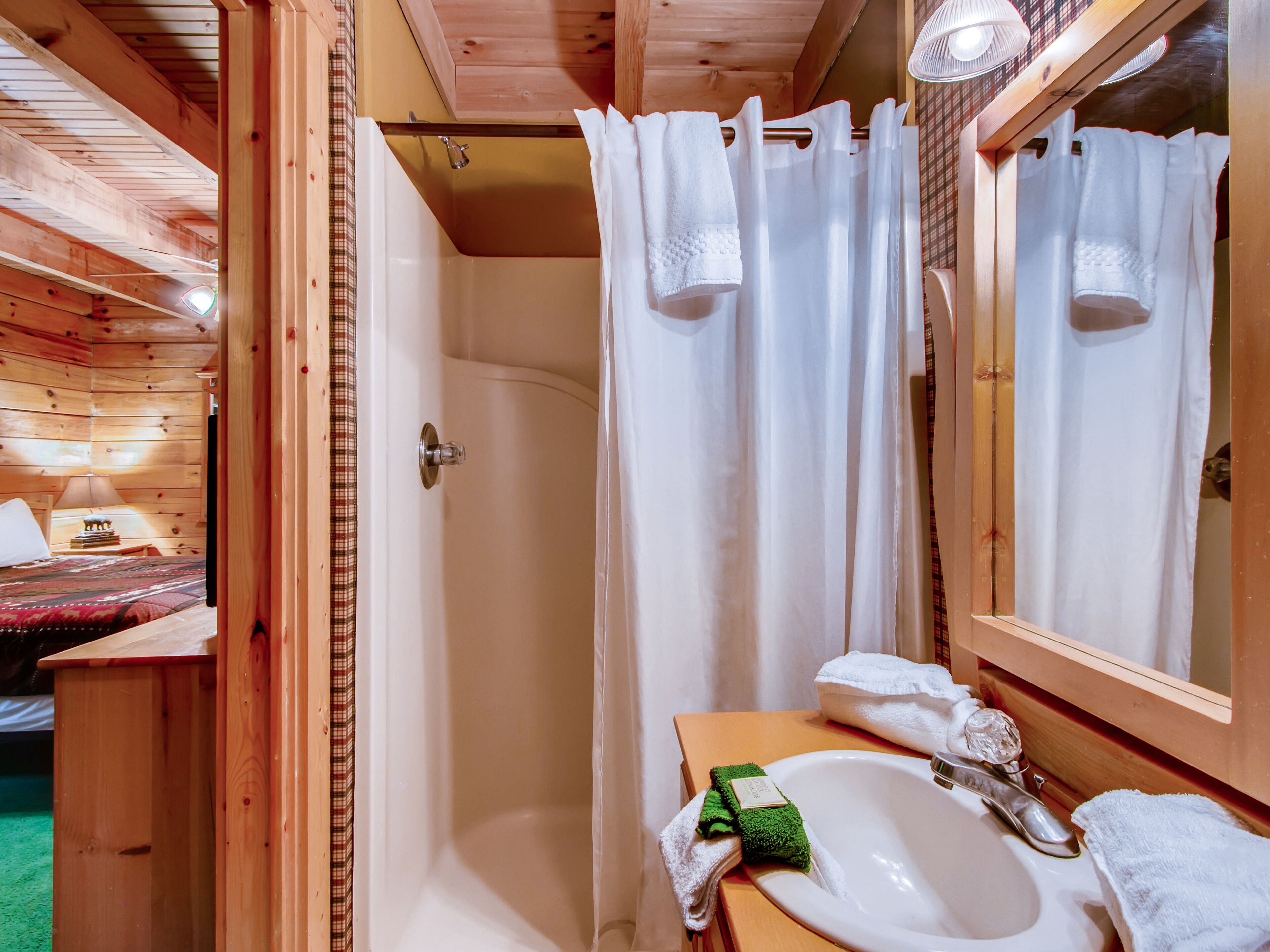 A wooden cabin bathroom with a shower, a sink, and a mirror.