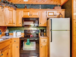 A kitchen with wooden cabinets, a microwave, a stove, a refrigerator, and a coffee maker. - Pet-Friendly | Hot Tub | Secluded | Jacuzzi (Sevierville)