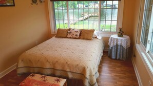 A bedroom with a large bed, a small table with a lace tablecloth, and a view of a lake through a window.