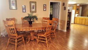 A dining area with a wooden table and chairs, a potted plant, and framed artwork on the wall.