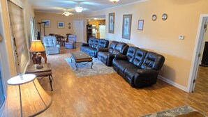 A living room with a sectional sofa, a coffee table, and a lamp. There is a door leading to another room.