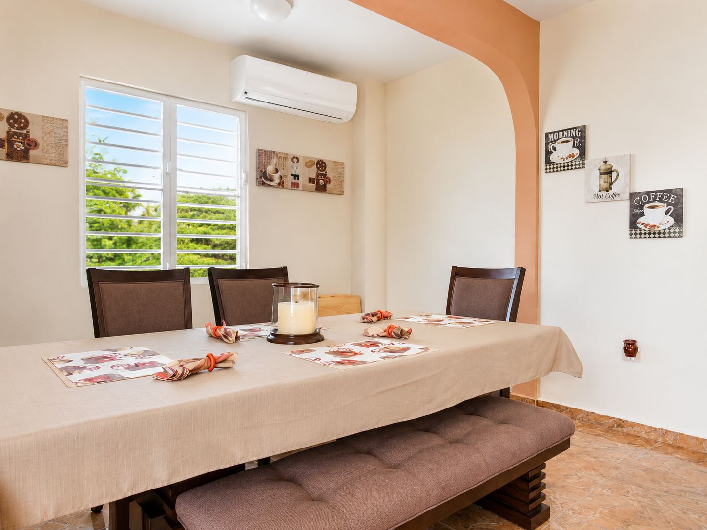 A dining area with a table set for four, a bench, and a wall-mounted air conditioner.