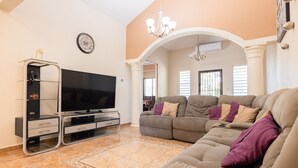 A living room with a flat-screen TV, a sectional sofa, and a glass cabinet. - Big vacational house in Isabela (Moca)