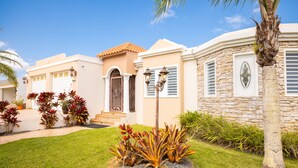 A residential building with a stone facade, a front entrance with a door and steps, and a small garden with plants and a palm tree. - Big vacational house in Isabela (Moca)