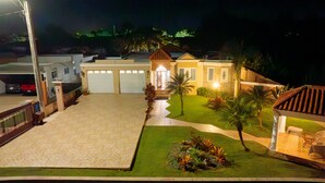 A well-lit residential property with a driveway, a garage, and a small garden with palm trees. - Big vacational house in Isabela (Moca)