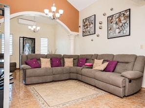 A living room with a sectional sofa, a chandelier, and abstract wall art. - Big vacational house in Isabela (Moca)