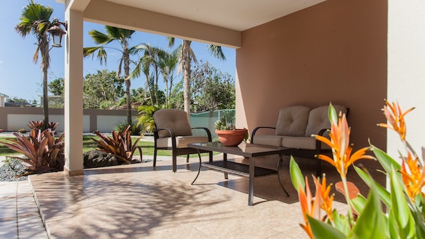 An outdoor patio area with two chairs and a table, surrounded by potted plants and palm trees. - Big vacational house in Isabela (Moca)