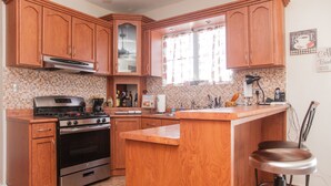A kitchen with wooden cabinets, a gas stove, an oven, a coffee station, and a window with curtains. - Big vacational house in Isabela (Moca)