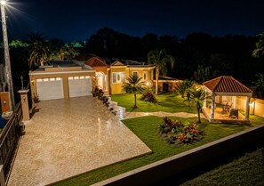 A residential property with a paved driveway, a covered outdoor seating area, and a well-maintained lawn. - Big vacational house in Isabela (Moca)