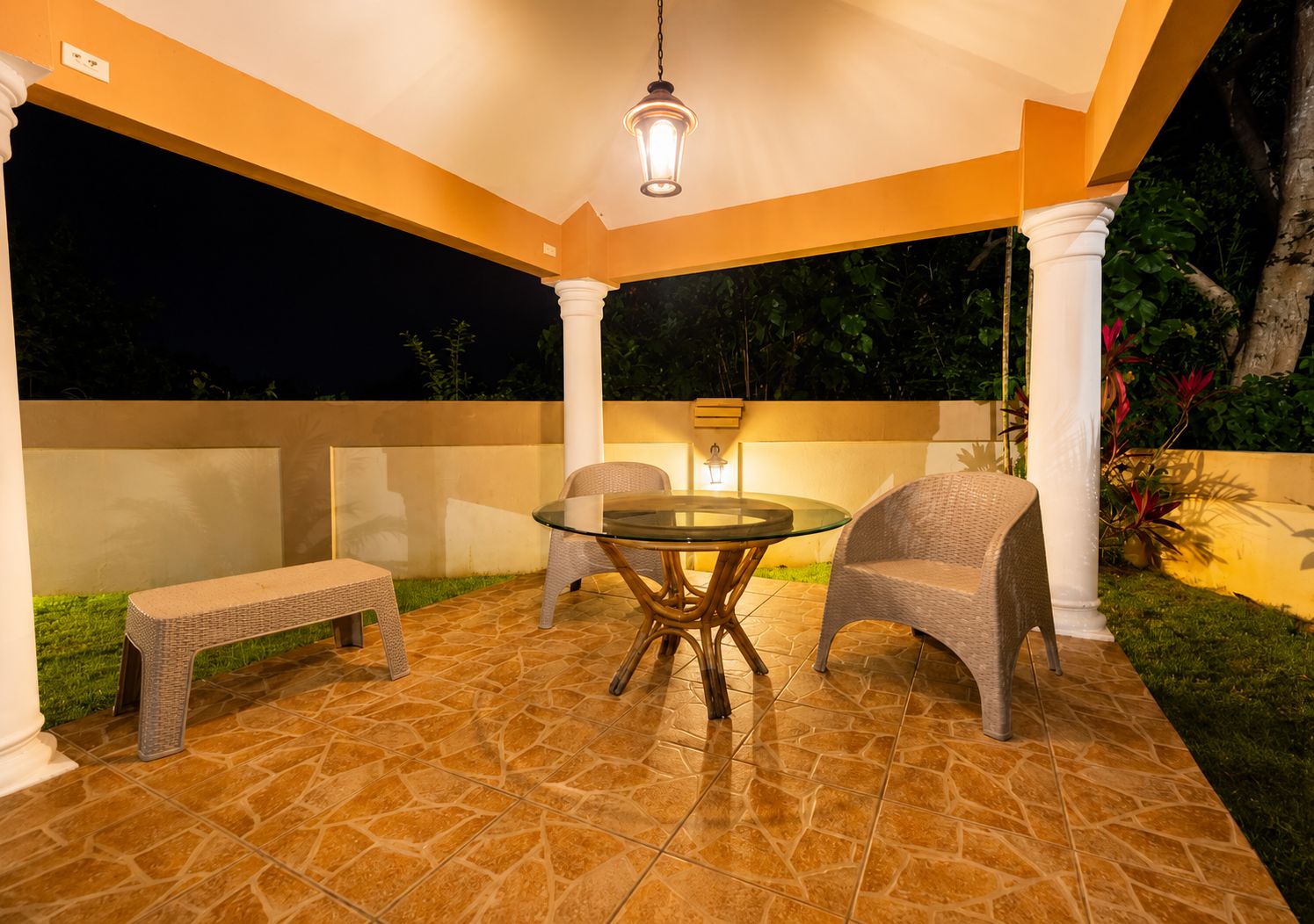 Un patio techado con una mesa redonda y dos sillas, un banco y un lámpara colgante.