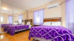 A hotel room with two beds, each covered with purple patterned bedspreads, a large mirror, an air conditioning unit, and a tiled floor. - Big vacational house in Isabela (Moca)