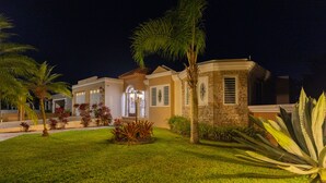 Una propiedad residencial bien iluminada, con jardín ajardinado, fachada de piedra y una entrada destacada con arco decorativo.